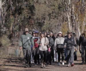 Group of people walking along a dirt path in a wooded park, smiling at the camera.